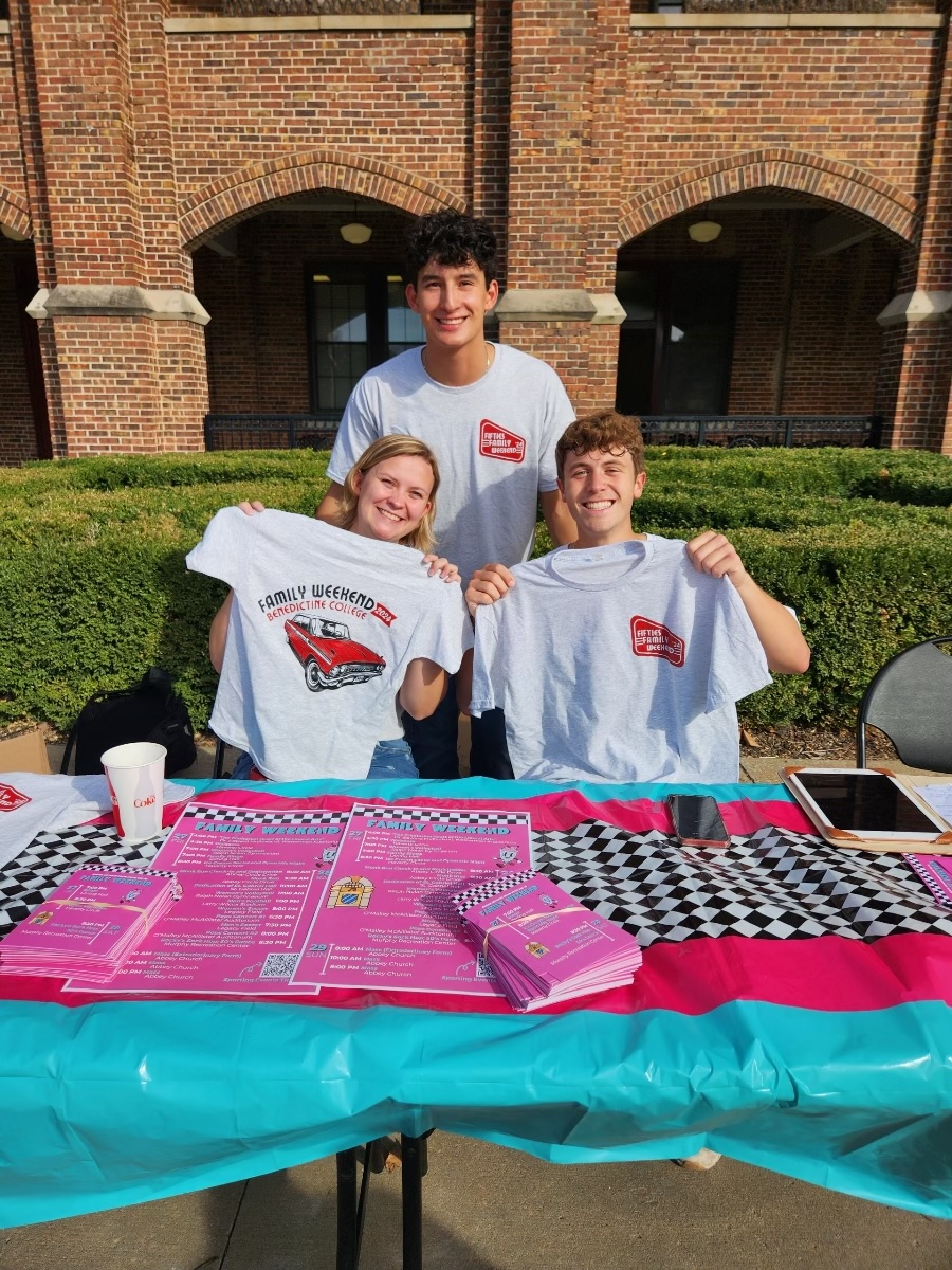 ⁃	Maggie Miller (left), Gabe Fuerte (middle), and Tobias Steffensmeier (right) sell t-shirts to promote Family Weekend